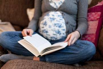 Low section of pregnant woman reading book on sofa at home