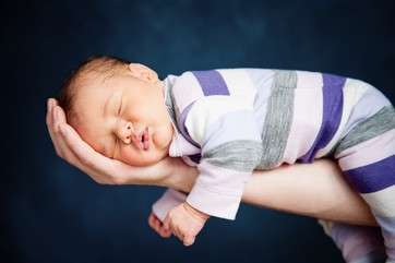Portrait of newborn baby girl lying on father's arm by .