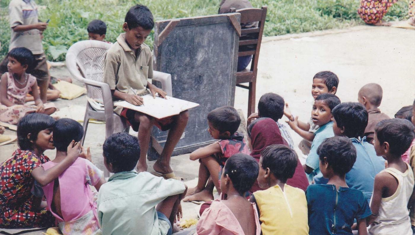 Babar Ali (seated in the chair) teaching ragpickers how to read and write at the age of 9 in the backyard of his home in Murshidabad, West Bengal. by .